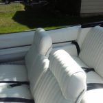 White leather interior of a classic convertible car with front and rear bench seats and black seat belts.