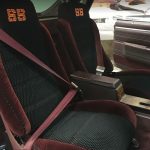 Two front car seats with "SS" logos, burgundy seat belts, and a center console inside a vintage vehicle.