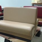 Beige restaurant booth seat in front of maroon booth seats inside a workshop with tools and materials visible.