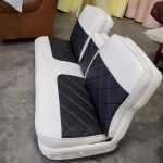 A two-tone black and white upholstered car bench seat with diamond-patterned stitching sits on a concrete floor.