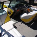 Interior of a speedboat with white and yellow seats, a steering wheel, dashboard controls, and a red fire extinguisher.