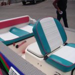 Colorful boat seats with teal, white, and pink upholstery, with part of a person standing nearby.