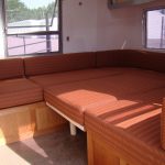 A built-in seating area with orange striped cushions forms a bed inside a camper or RV with open windows.