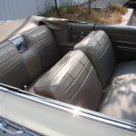Interior of a vintage convertible car with beige leather seats and top down, parked near a curb and some grass.