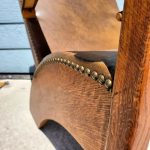 Close-up of a wooden chair with brown leather upholstery and brass stud detailing, positioned outdoors on concrete.