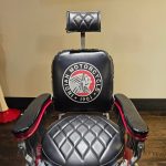 Vintage-style black chair with "Indian Motorcycle 1901" logo on the backrest, featuring armrests and a headrest.