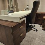 Modern office desk with a leather chair, three-drawer cabinet, and small decor on a patterned carpet.