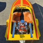 Overhead view of a yellow and orange speedboat with two leather seats and an exposed engine at the rear.