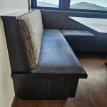 Dark wood booth bench with gray upholstered seat and backrest, next to a table and window with a mountain view.