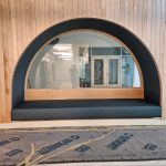 A built-in arched bench with a glass window in a wood-paneled wall, construction materials on the floor.
