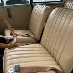 Tan leather seats and brown seat belts inside a vintage car, with part of a white car visible outside the window.