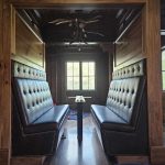 Two black leather booth seats with a small table between them in a wooden-paneled room, facing a window.