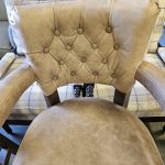 Tan leather chair with button-tufted backrest and cushioned seat, placed in front of a plaid-upholstered chair.