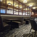 Empty restaurant booths with black tables and brown seats, separated by glass partitions under ceiling lights.